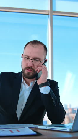 confident business person talking the phone in office. portrait of a boss sitting at table and dealing business problems through the phone. vertical video