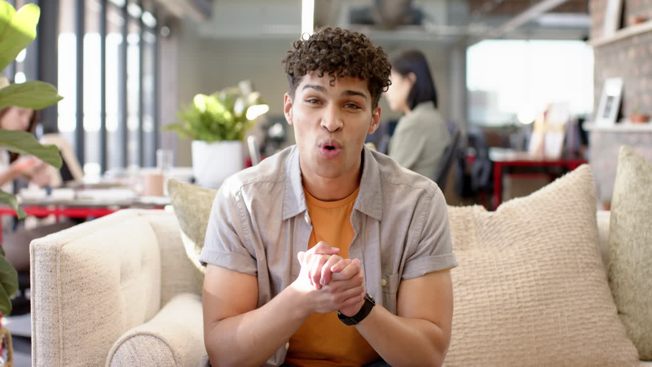 On video call, smiling man on couch, gesturing while talking in modern living room, at office