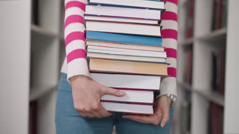 heavy textbook pile in woman hands closeup. bookworm carries huge stack of literature walking across library. librarian works with books in storage