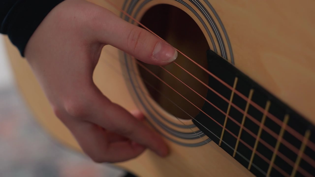 Closeup of hand strumming guitar strings, precise fingerpicking motion over soundhole with warm wood texture, soft background blur suggests home practice and tutorial focus on technique and tone