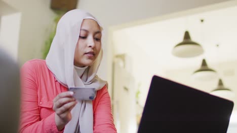 video of smiling biracial woman in hijab making online payment using laptop and credit card at home