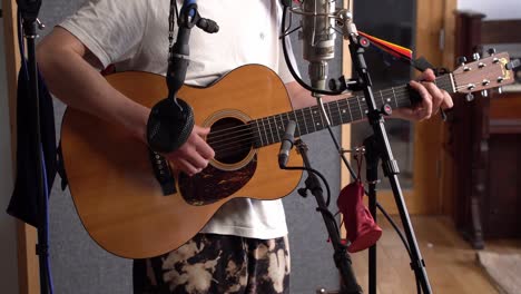 shot of a fingerstyle musician playing an acoustic guitar in a recording studio