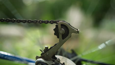 close-up of bicycle's chain and gear system in motion as the wheel rotates briefly, the chain and cogwheel are in sharp focus, while the blurred greenery in the background