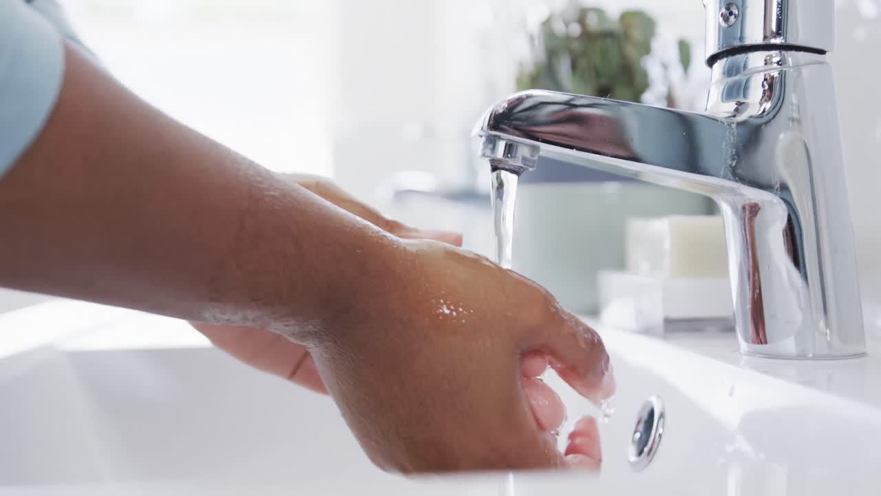 sección media de una mujer afroamericana enjuagando las manos a fondo en el fregadero del baño, en cámara lenta
