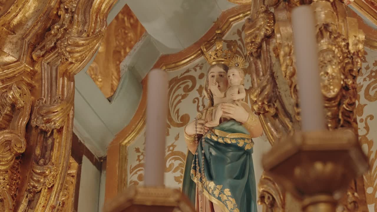 Close up of a Virgin Mary and Child statue surrounded by intricate golden baroque decorations inside a church altar