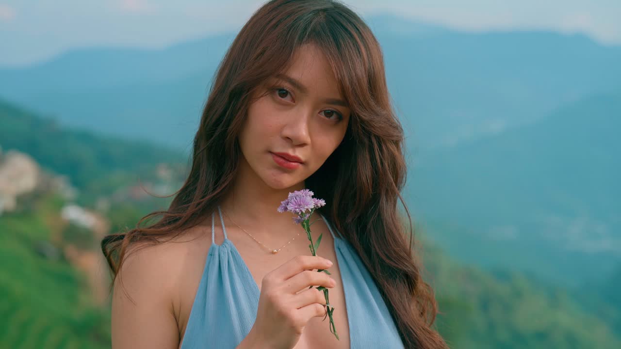 山を背景に屋外で紫色の花を持つ若い女性