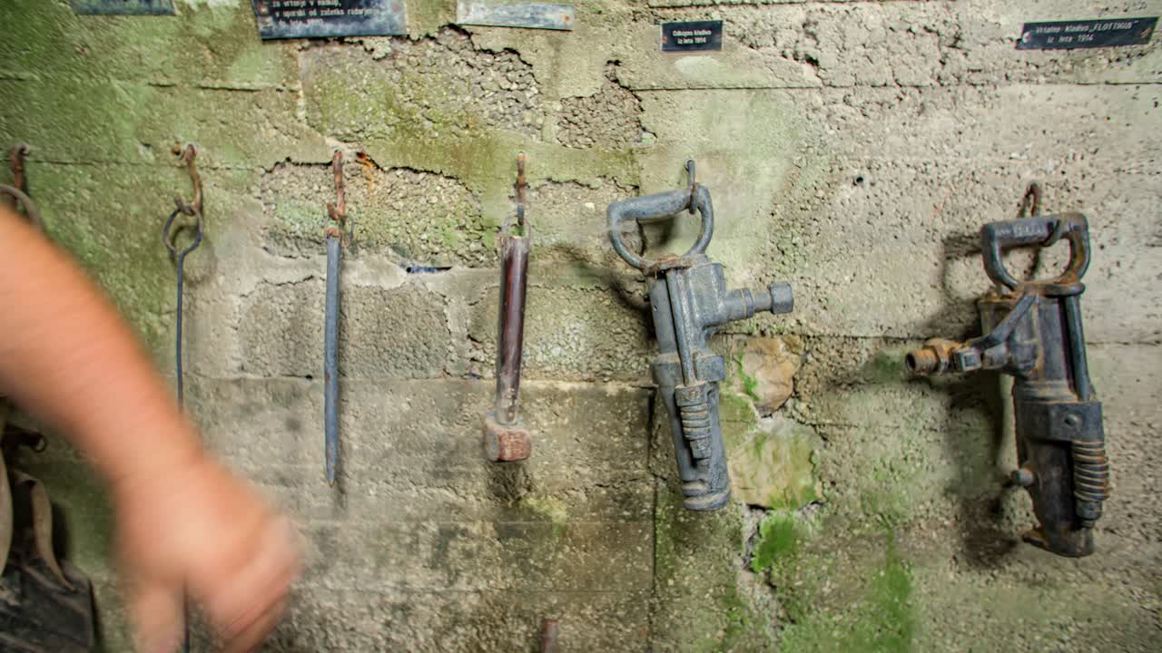 A man's hand putting an old rusty hammer to other antique tools, hanging on a wall in museum display