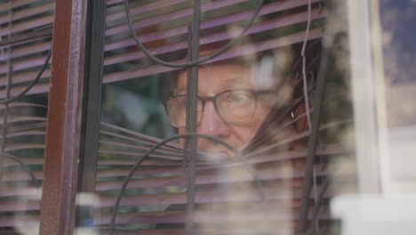 un anciano con gafas abre las persianas y mira por la ventana, desde afuera