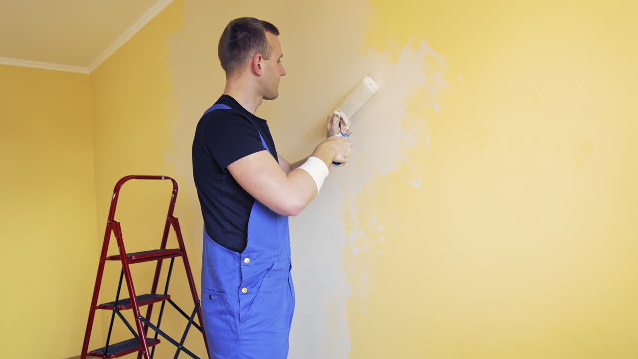 Young worker painting wall in room. Offering professional painting services.
