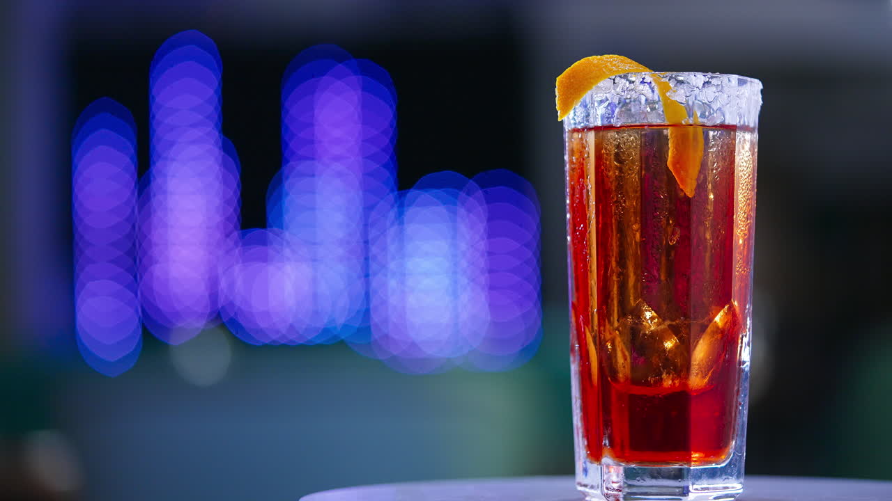 Little rotating table with red beverage. Beautiful cocktail with salt on glass top and orange peel. Close up. Blurred backdrop.
