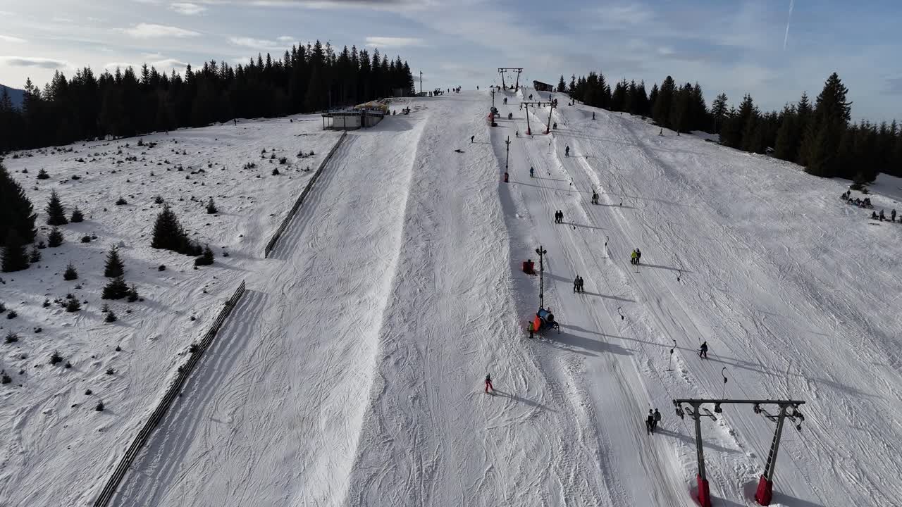 Vista aerea con drone di una pista da sci innevata in montagna con persone che sciano e fanno snowboard in una soleggiata giornata invernale. Concetto di sport invernali, turismo e attività ricreative all'aperto