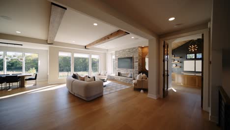 a spacious open-plan living room with large windows, wooden beams, and a stone fireplace, connected to a dining area
