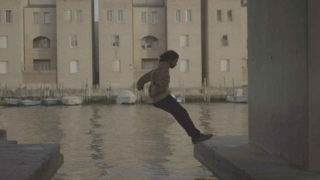 Person Jumping and Sitting by a Canal in Venice