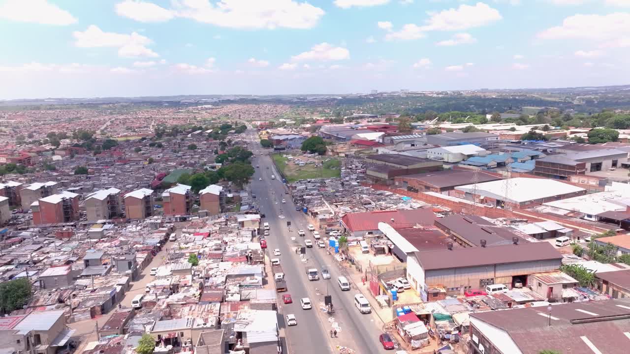 Aerial panning shot over Alexandra Township, Johannesburg, South Africa, on a sunny day with scattered clouds and cars moving on main road