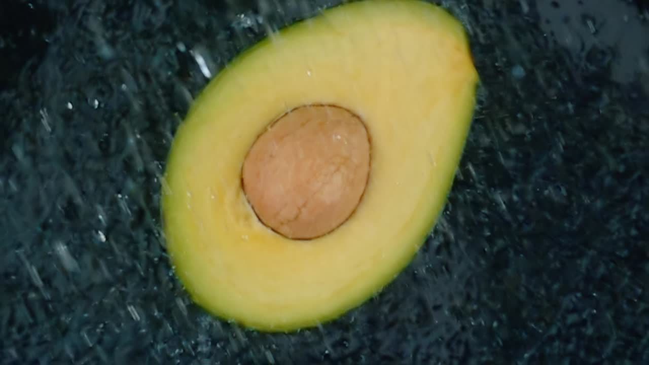 검은 바탕에  ⁇ 은 물 스플래시와 함께 아보카도. 슈퍼 슬로우 모션 루프.
