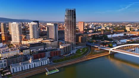 Multiple modern buildings at the waterfront of the Danube. Drone footage at the Appolo Bridge in Bratislava, Slovakia at sunset time