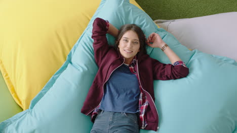 top-view-happy-caucasian-woman-student-jumping-on-colorful-pillows-smiling-relaxing-female-resting-enjoying-lunch-break-in-trendy-office-workplace
