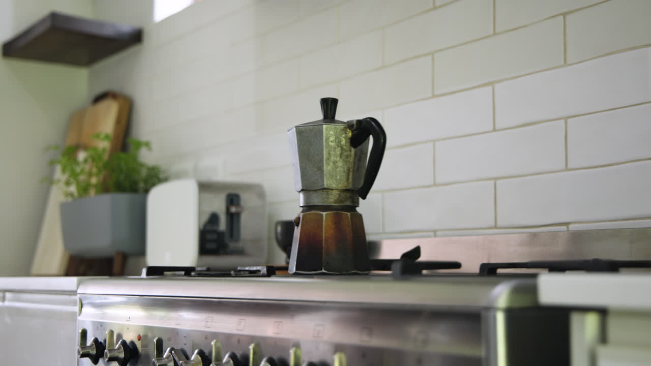 Moka pot brewing coffee on kitchen stove with herbs in background, at home