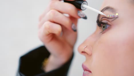 close-up of a woman applying glitter and rhinestones as part of creative eye makeup