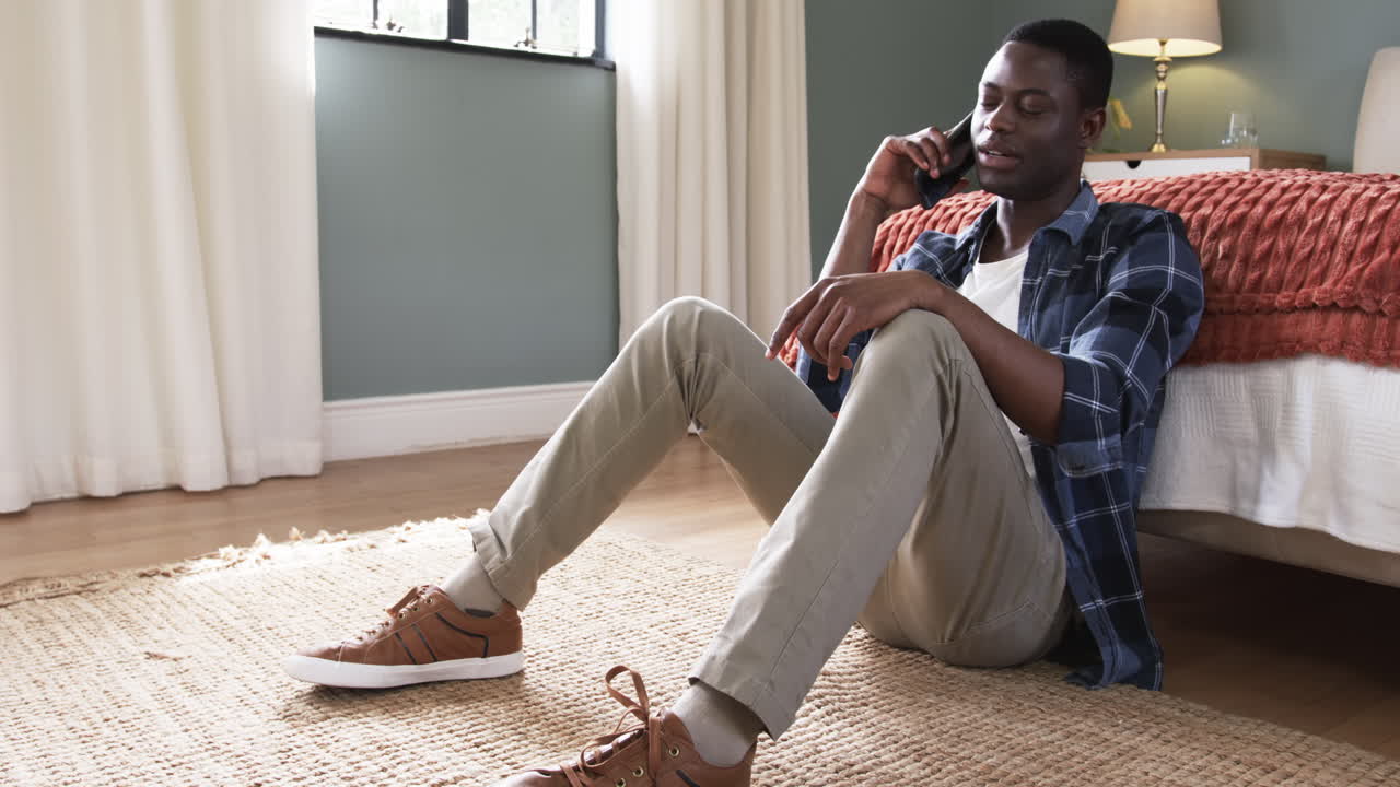 Relaxing at home, young man talking on smartphone, sitting on floor