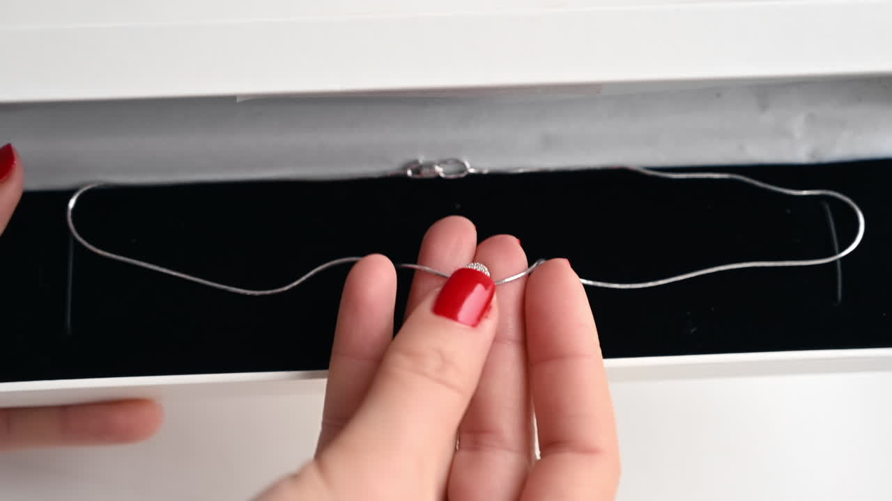 Close view of a woman holding necklace with diamonds. Box, hands with red nails
