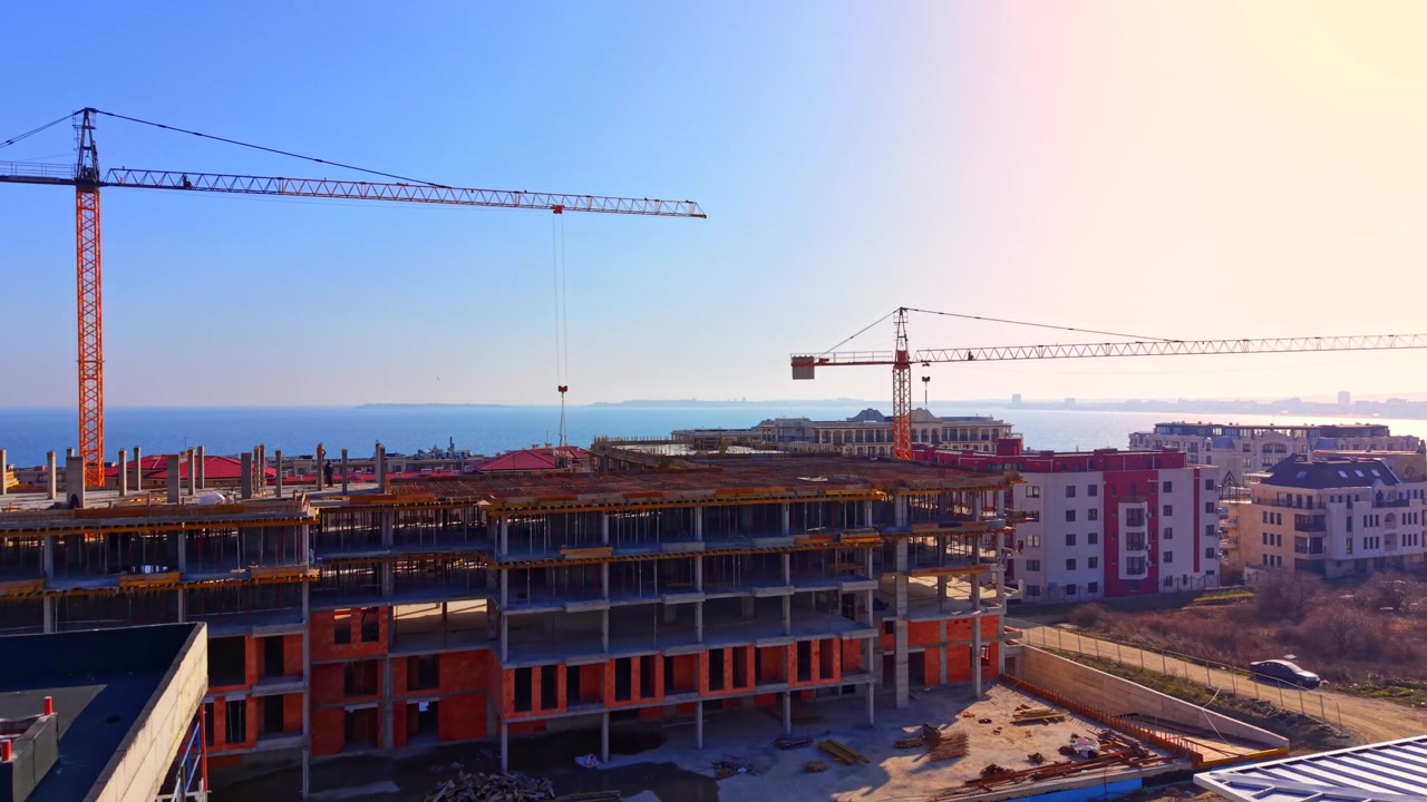 Vista elevata all'orizzonte di uno sviluppo residenziale/resort a più livelli con mare e costa distante sullo sfondo. Due gru a torre in funzione in un cantiere costiero, Bulgaria