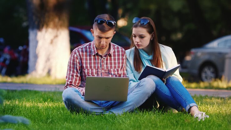 amici di un uomo e di una donna seduti sull'erba nel parco che si godono il portatile sullo sfondo