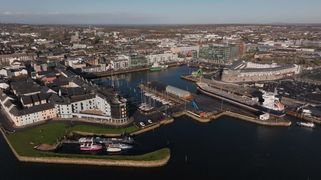 Metraje de dron en picada mostrando el pintoresco puerto de Galway con barcos, apartamentos modernos y el horizonte urbano de la ciudad de Galway en Irlanda en un día despejado.