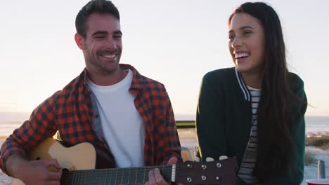feliz pareja caucásica sentada en un buggy de playa junto al mar tocando la guitarra