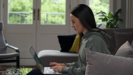 anxious woman sitting indoors on sofa working from home using laptop worried about cost of living crisis