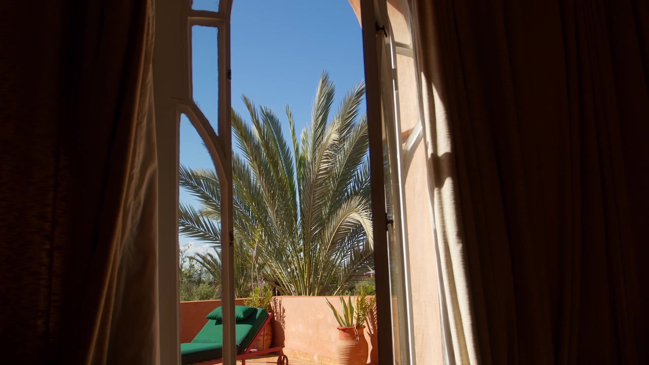 Le porte aperte della villa rivelano una terrazza soleggiata con palma e lettino all'esterno