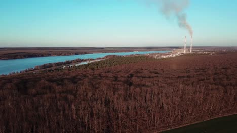 Aerial view of winter forest without snow against a background of a power station. Beautiful nature river