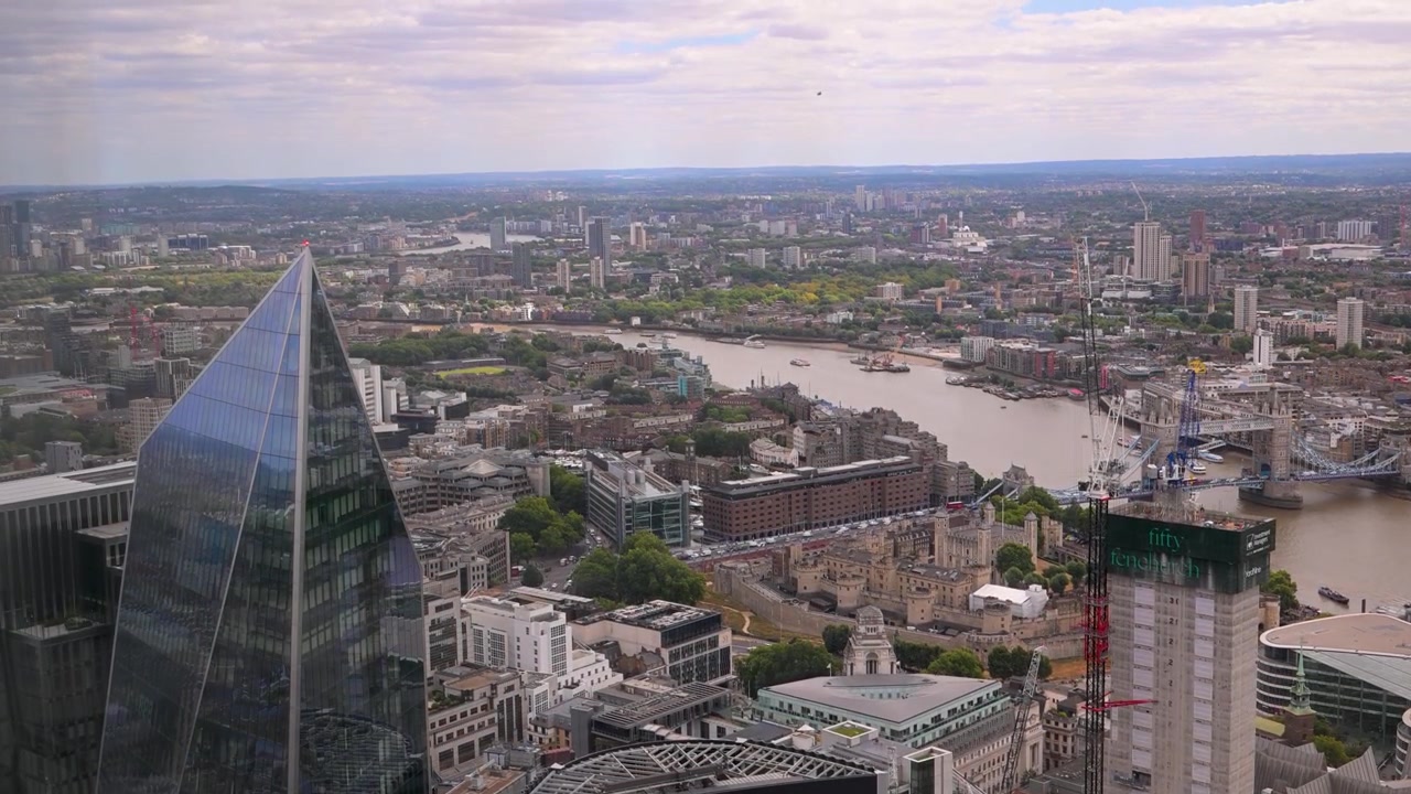 Widok z lotu ptaka na Tamizę z wieżą The Scalpel, Tower of London i odległą panoramą miasta w pochmurny dzień.