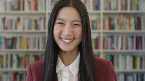 close up portrait of cute young asian woman student smiling happy looking at camera in public library bookshelf background