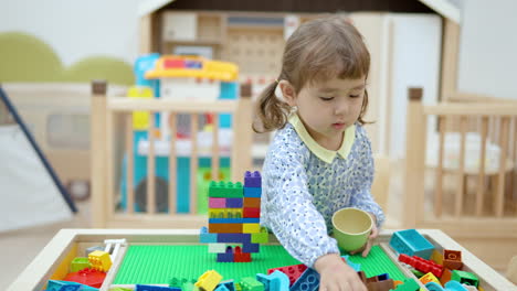 enthusiastic little girl playing with building blocks bricks making tower wall at childcare room