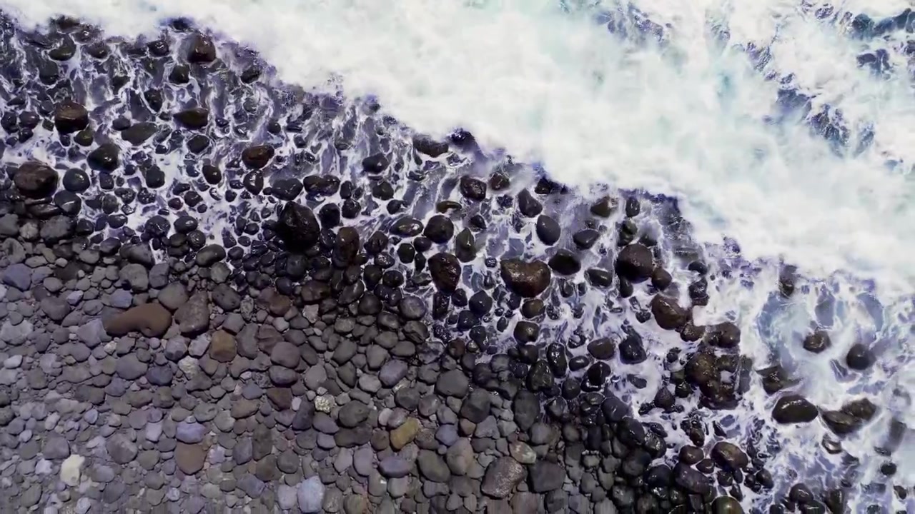 Onde si infrangono su rocce vulcaniche lungo una costa rocciosa, viste dall'alto alla luce del giorno.