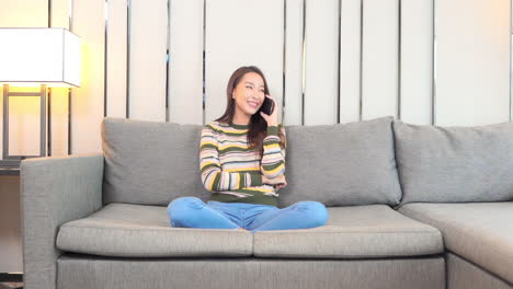 A-pretty-young-woman-makes-a-call-on-her-smartphone-while-sitting-on-a-huge-sectional-in-a-modern-hotel-room