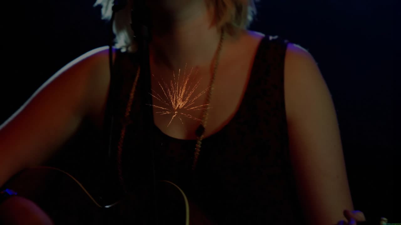 Musician strumming guitar on stage causing spark light while camera rising revealing singing at mic