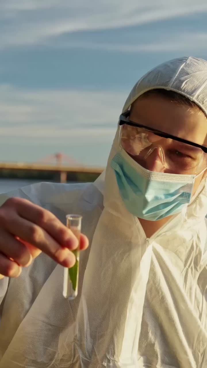 Close vertical de um inspetor usando máscara enquanto examina uma amostra ambiental ao ar livre, agita e inclina um tubo de ensaio com uma planta