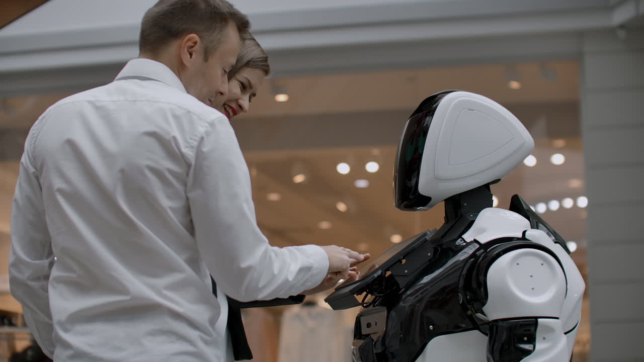 dos personas un hombre y una mujer se comunican con un robot. presiona el robot con las manos en la pantalla. un asistente robot interactuando en un centro comercial con una pareja. asistente robot en el piso de negociación