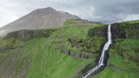 aerial view of a waterfall in iceland during summer, with green grass covering the landscape and mountains in the background