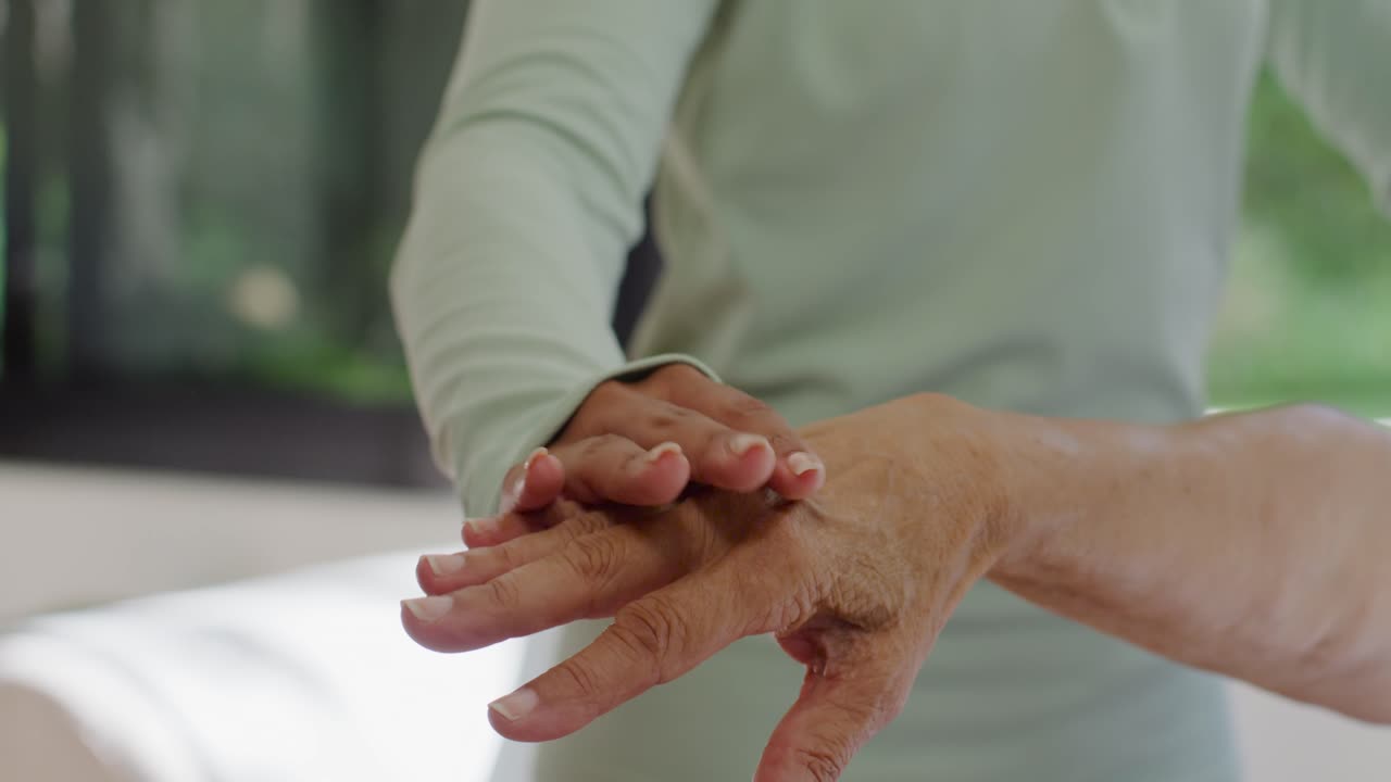 Badante che posiziona la mano sul polso e sul dorso della mano dell'anziano, massaggiando le dita a casa per terapia