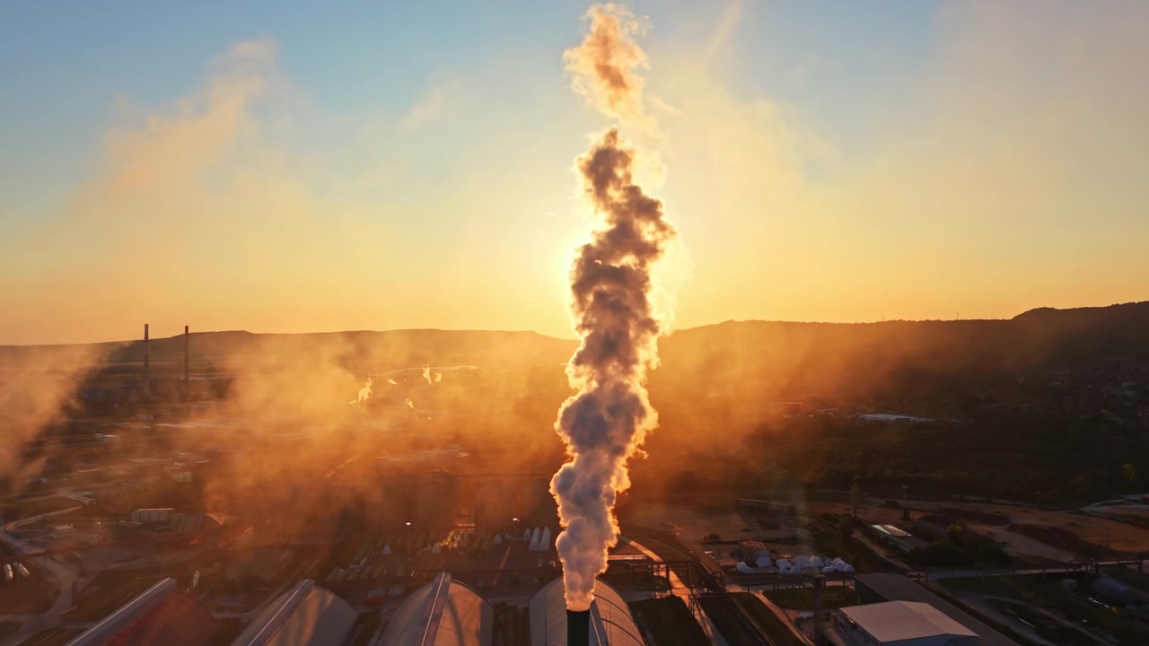 Rookpluimen uit een fabriek bij zonsondergang met de zon schijnend op de achtergrond