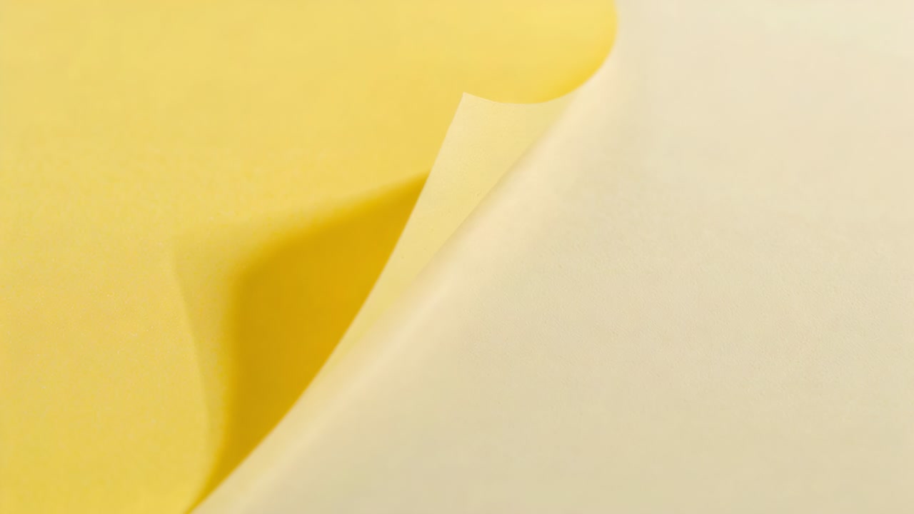 Peeling cream sheet lifting from top-right, revealing yellow layer in studio for color contrast