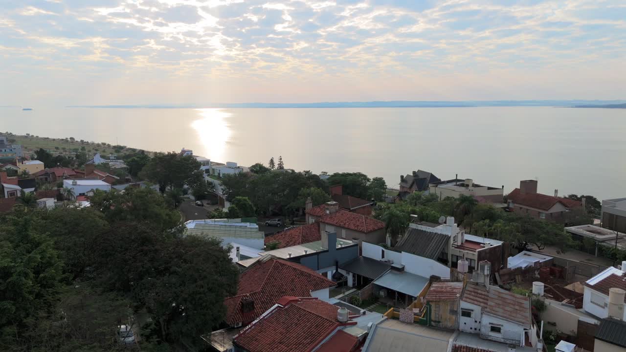 Descending drone flyover above Mediterranean style houses and river at sundown in Posadas, Argentina overlooking the horizon
