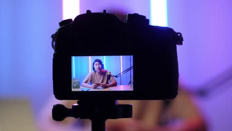 display camera of asian man holding mobile phone and talking to camera while live stream