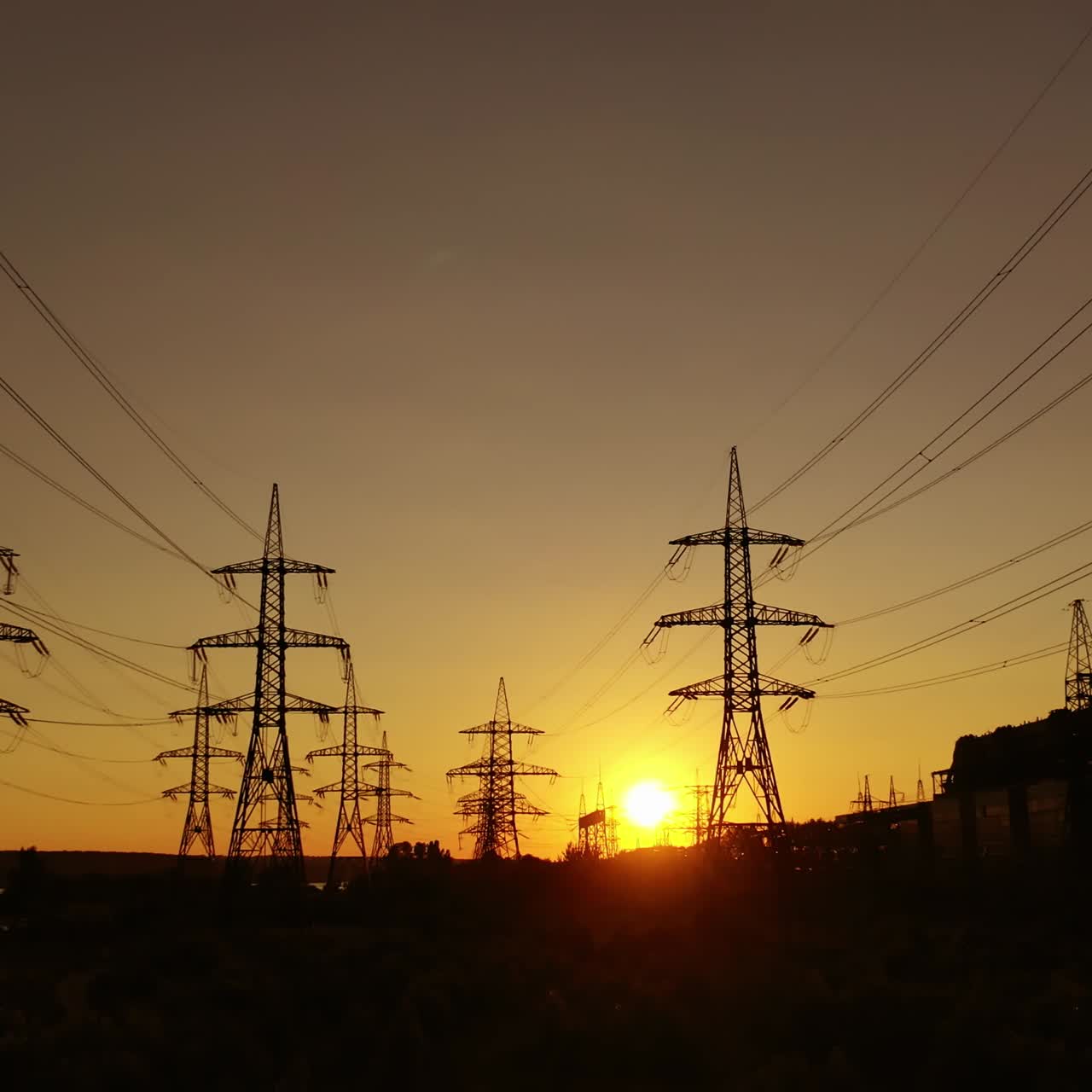 Transmission towers at dusk. Electric pylons near the smoking industrial pipe in the evening. Electric high voltage lines against beautiful orange sky at sunset. Energy efficiency conception.