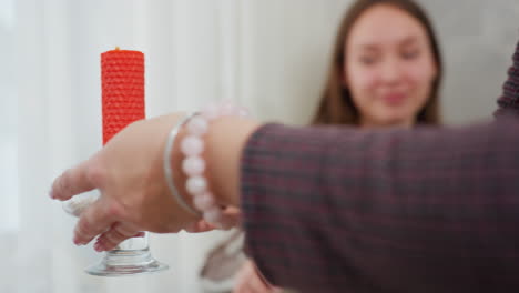 primer plano de una mujer colocando delicadamente una elegante vela roja en un soporte de vidrio en la mesa mientras se prepara para el desayuno, la mano adornada con un hermoso brazalete de cuentas