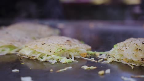 savoury japanese pancakes, okonomiyaki being served on hot grill, close pan shot