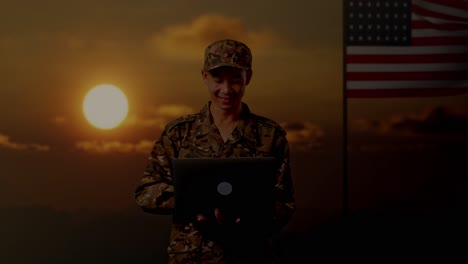 soldado trabajando en una computadora portátil durante el atardecer con la bandera estadounidense